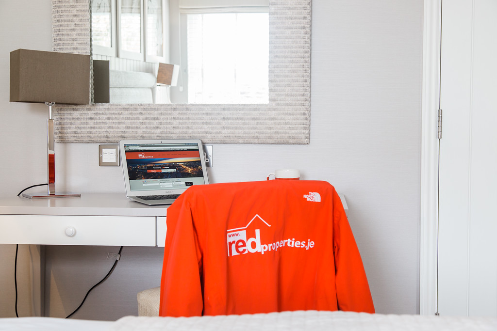 open laptop at a desk and a chair with red properties branded jacket